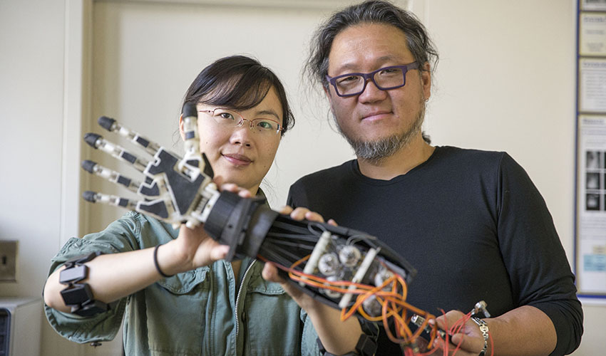 doctors okada and zhang hold robotic arm they've created